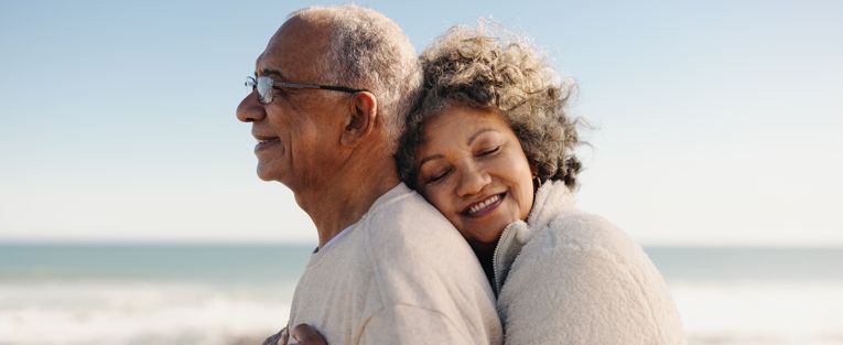 senior-woman-hugs-her-man-on-the-beach